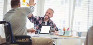 Man at desk high fiving his friend with laptop